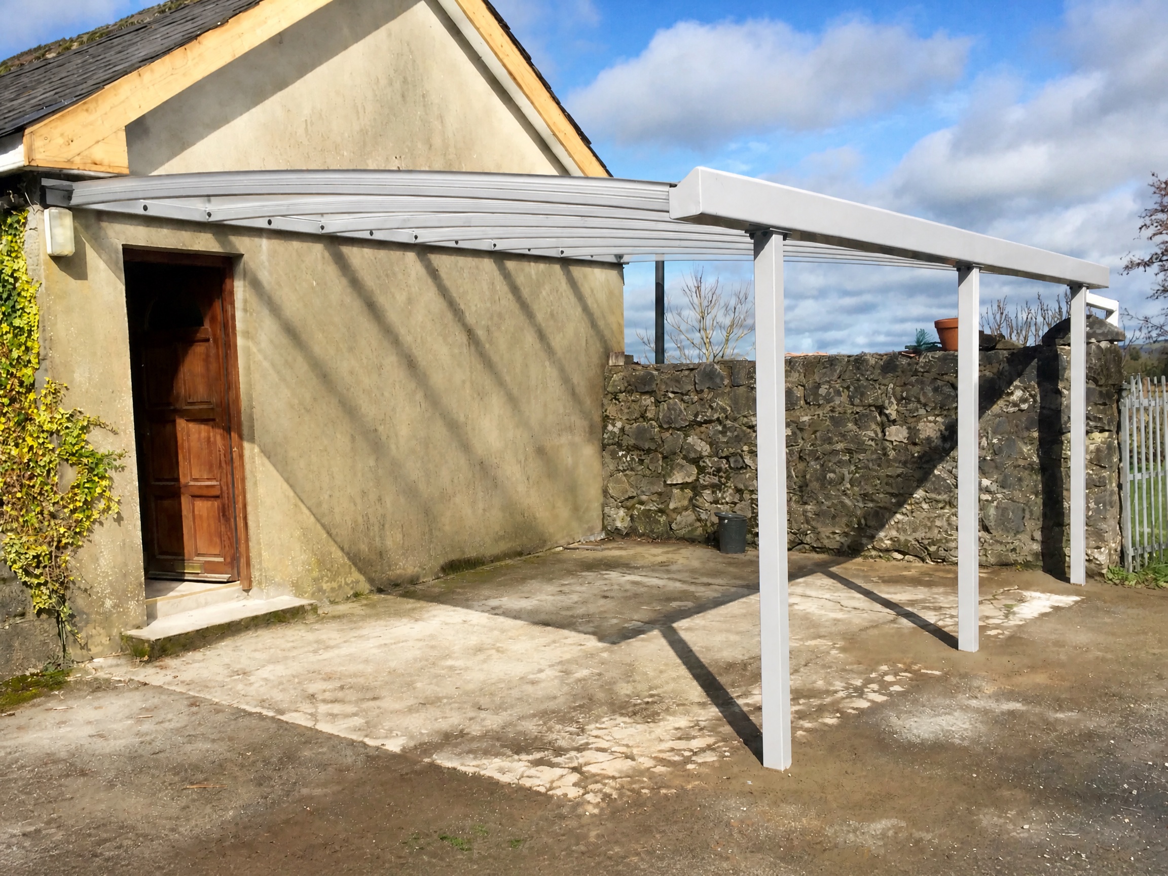 White open-sided carport installed alongside a stone house